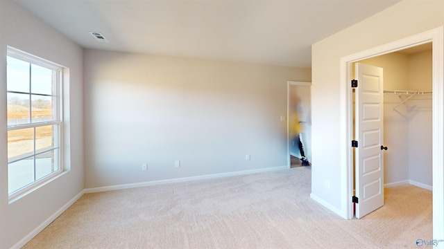 unfurnished bedroom featuring a closet, a walk in closet, and light carpet