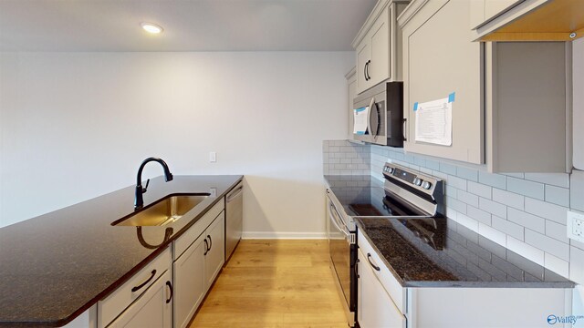 kitchen featuring stainless steel appliances, tasteful backsplash, dark stone countertops, sink, and light hardwood / wood-style floors