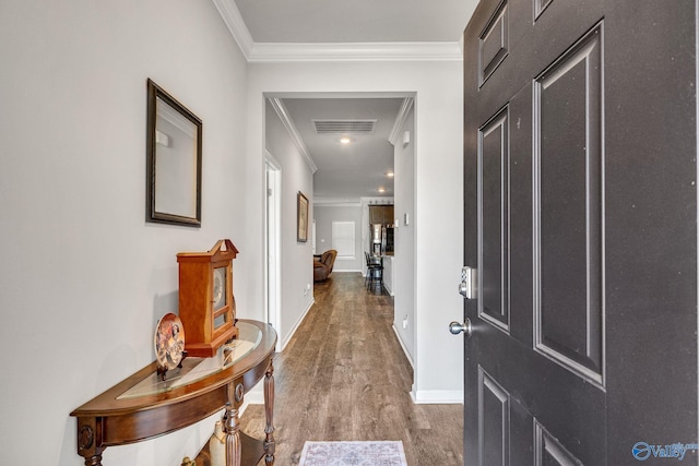 hallway with ornamental molding, wood finished floors, visible vents, and baseboards