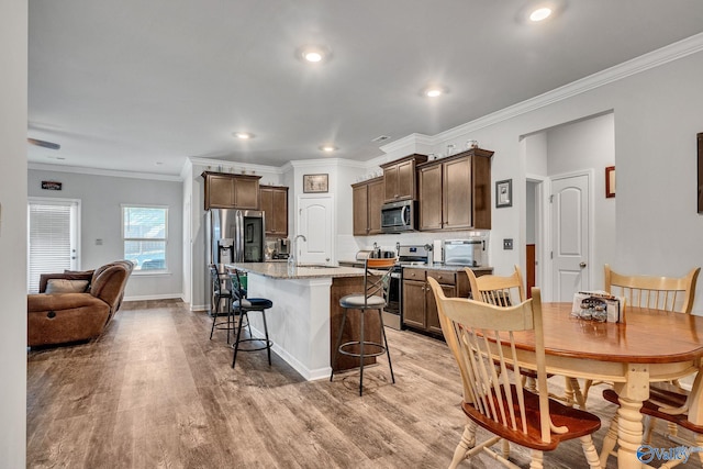 kitchen featuring light stone counters, a kitchen island with sink, a sink, appliances with stainless steel finishes, and a kitchen bar