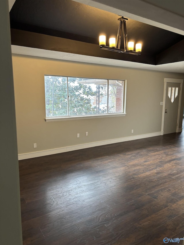 unfurnished room featuring a raised ceiling, plenty of natural light, dark hardwood / wood-style floors, and an inviting chandelier