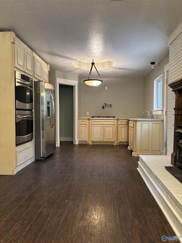 kitchen with appliances with stainless steel finishes, hanging light fixtures, dark wood-type flooring, and cream cabinets