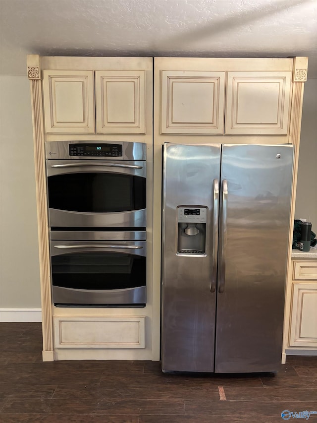 kitchen with cream cabinetry, a textured ceiling, stainless steel appliances, and dark wood-type flooring