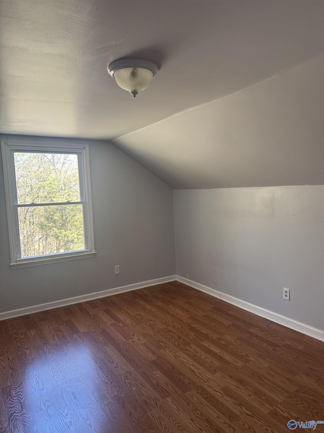 additional living space featuring baseboards, lofted ceiling, and dark wood-style floors