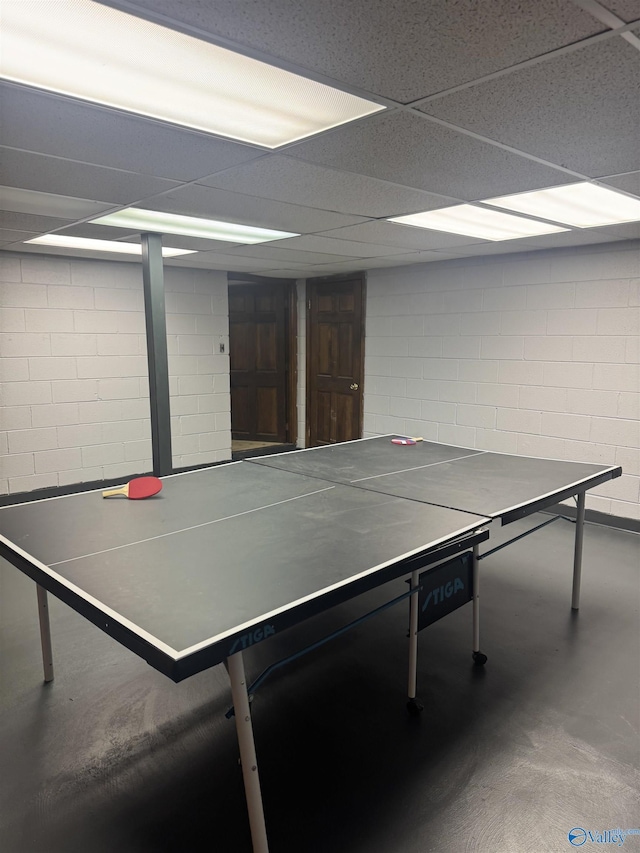 rec room with a drop ceiling, concrete block wall, and concrete flooring