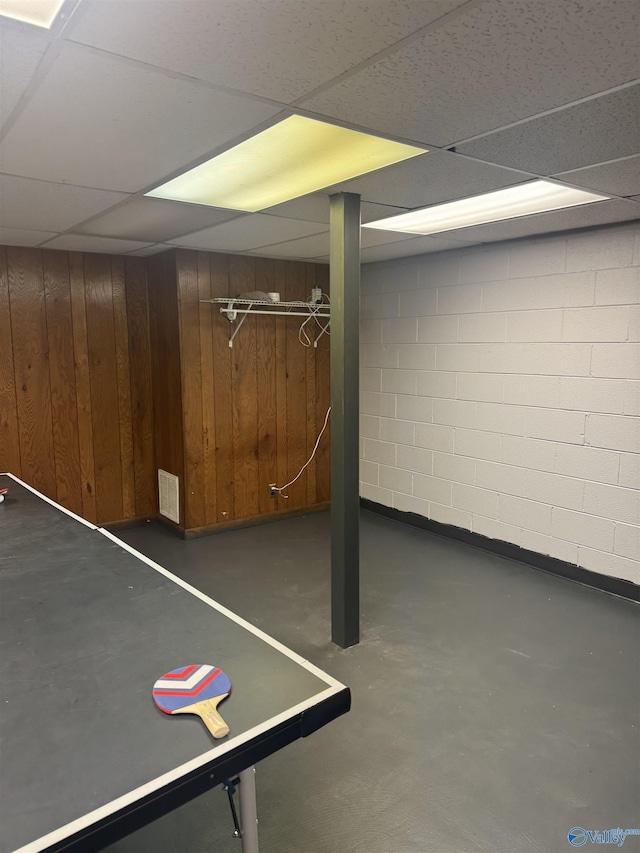 game room featuring concrete block wall, a paneled ceiling, wood walls, and concrete floors