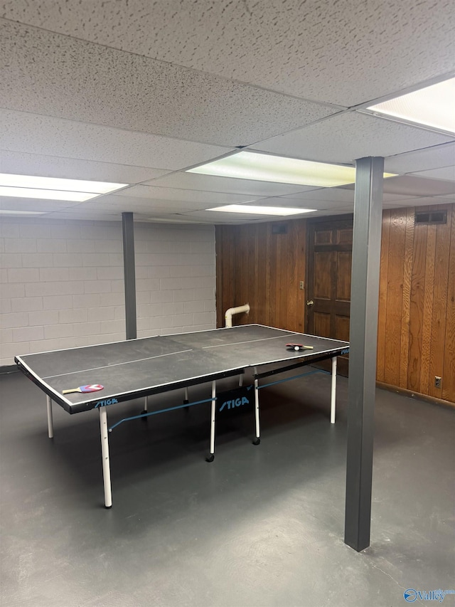 playroom featuring a drop ceiling, wooden walls, concrete flooring, and concrete block wall