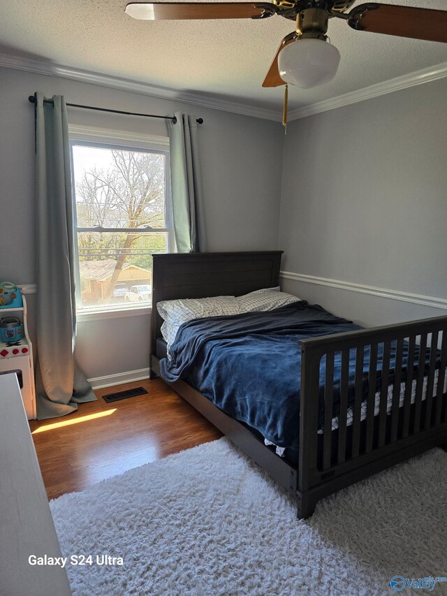 bedroom with crown molding, wood finished floors, visible vents, and a textured ceiling