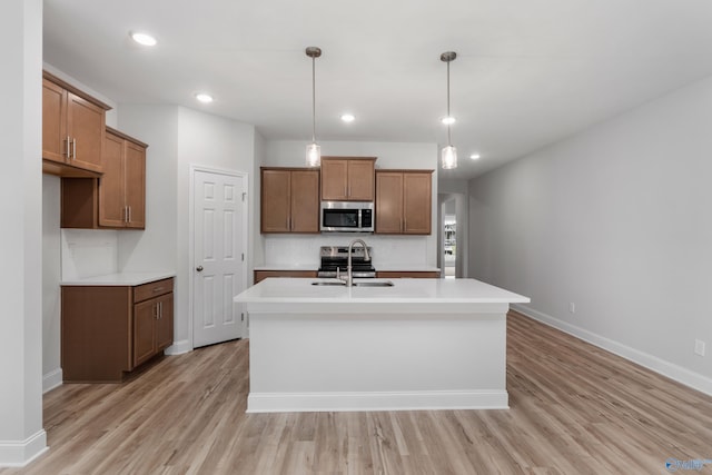 kitchen with appliances with stainless steel finishes, sink, hanging light fixtures, a kitchen island with sink, and light hardwood / wood-style flooring