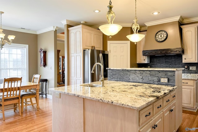 kitchen featuring light brown cabinetry, hanging light fixtures, stainless steel refrigerator, and a center island with sink