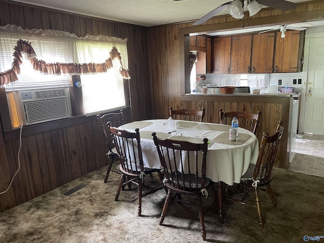 carpeted dining area featuring a textured ceiling, wood walls, visible vents, ceiling fan, and cooling unit