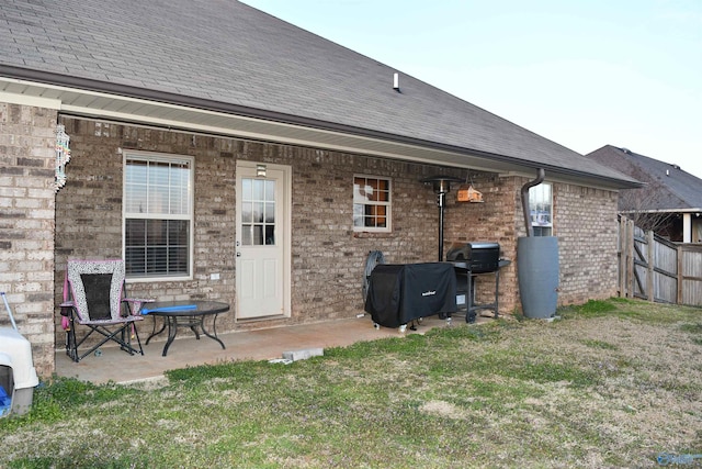 rear view of property featuring roof with shingles, a patio area, brick siding, fence, and a lawn