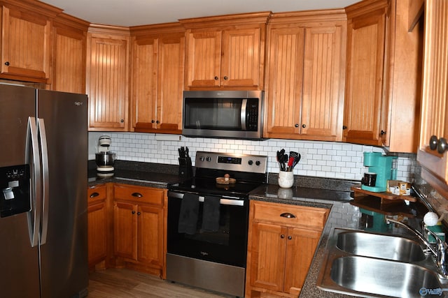 kitchen featuring brown cabinets, decorative backsplash, a sink, and stainless steel appliances