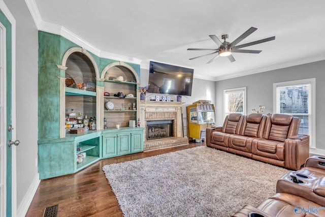 living room featuring crown molding, a brick fireplace, dark hardwood / wood-style floors, and ceiling fan