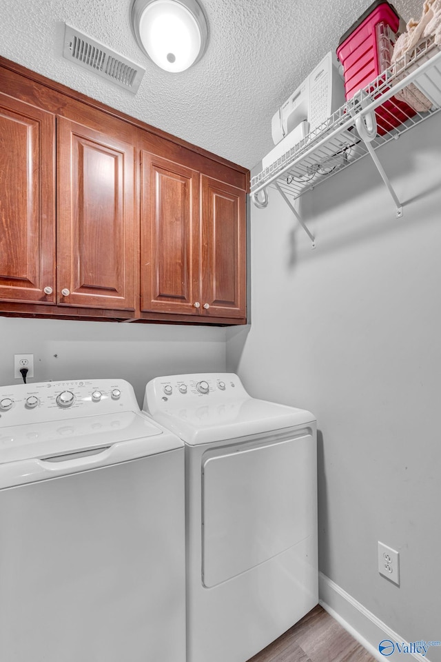 washroom featuring cabinets, light hardwood / wood-style flooring, a textured ceiling, and washing machine and clothes dryer