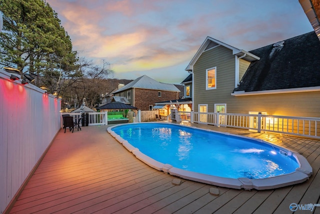 pool at dusk featuring a gazebo and a deck