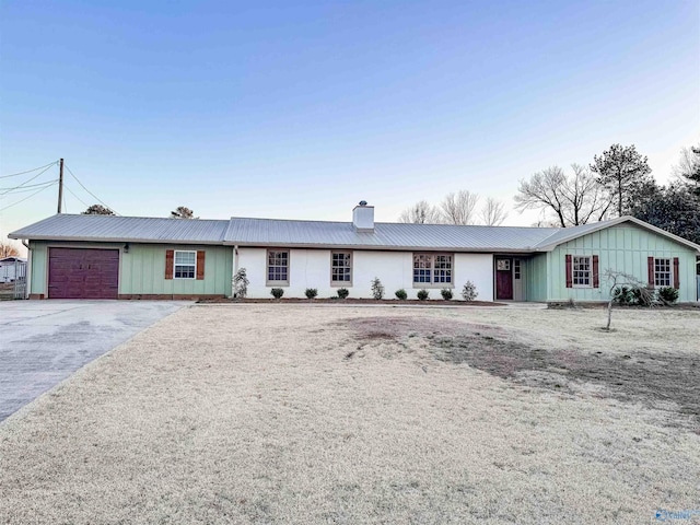 ranch-style house with aphalt driveway, a chimney, an attached garage, board and batten siding, and metal roof