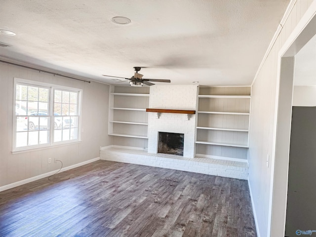 unfurnished living room with a textured ceiling, ceiling fan, built in shelves, wood finished floors, and a brick fireplace