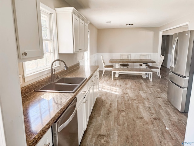 kitchen featuring stainless steel appliances, a sink, white cabinets, light wood-style floors, and dark stone counters