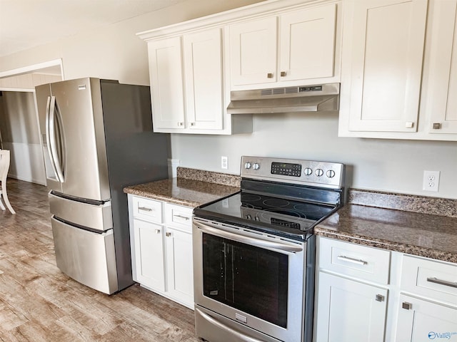 kitchen featuring under cabinet range hood, stainless steel appliances, white cabinetry, light wood finished floors, and dark stone countertops