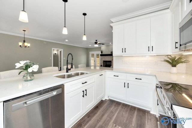 kitchen with kitchen peninsula, stainless steel appliances, sink, pendant lighting, and white cabinets