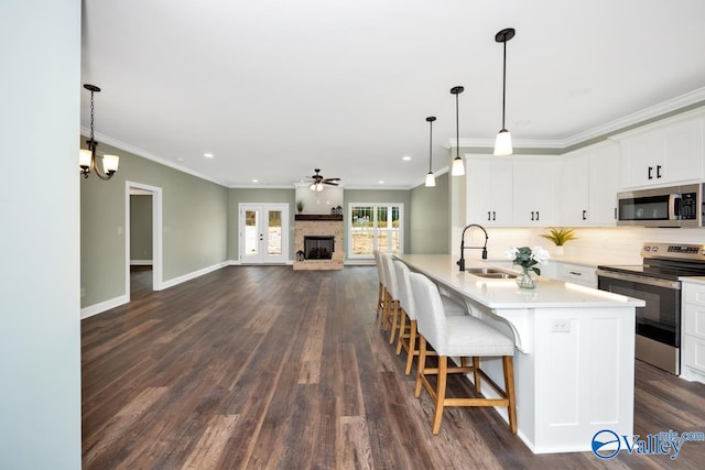 kitchen featuring a stone fireplace, stainless steel appliances, sink, white cabinetry, and dark hardwood / wood-style flooring