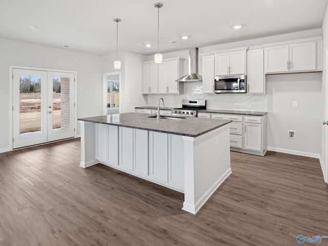 kitchen with wall chimney exhaust hood, white cabinetry, an island with sink, and stainless steel appliances