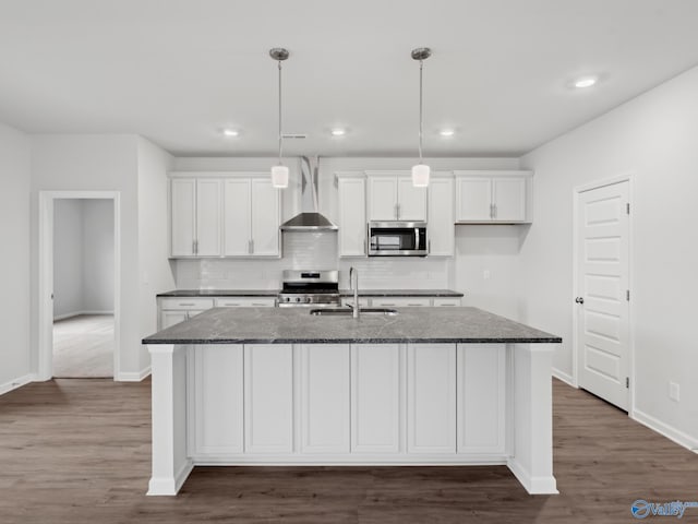 kitchen featuring dark stone counters, a center island with sink, sink, white cabinetry, and stainless steel appliances