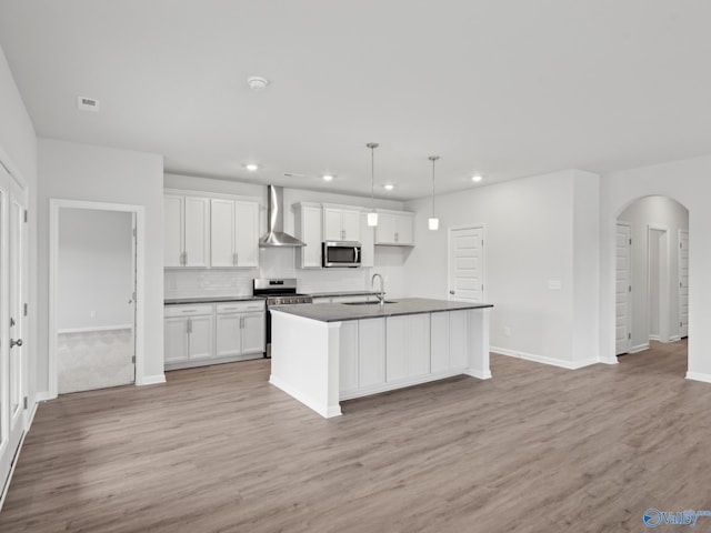 kitchen featuring appliances with stainless steel finishes, wall chimney exhaust hood, sink, a center island with sink, and white cabinets