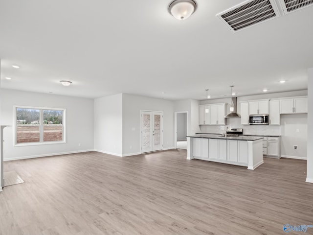 kitchen with a center island with sink, white cabinetry, light hardwood / wood-style floors, and wall chimney range hood