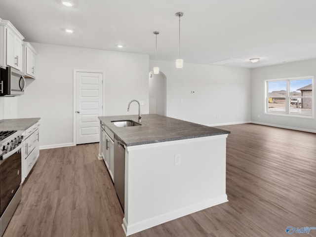 kitchen featuring stainless steel appliances, sink, white cabinetry, hanging light fixtures, and an island with sink