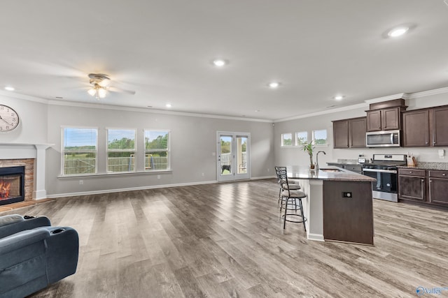 kitchen featuring appliances with stainless steel finishes, light wood-type flooring, a kitchen breakfast bar, a stone fireplace, and an island with sink