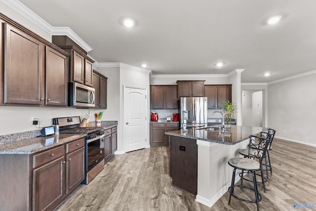 kitchen with dark brown cabinetry, sink, light hardwood / wood-style flooring, a center island with sink, and appliances with stainless steel finishes