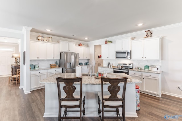 kitchen with white cabinets, a center island with sink, decorative backsplash, appliances with stainless steel finishes, and a breakfast bar area