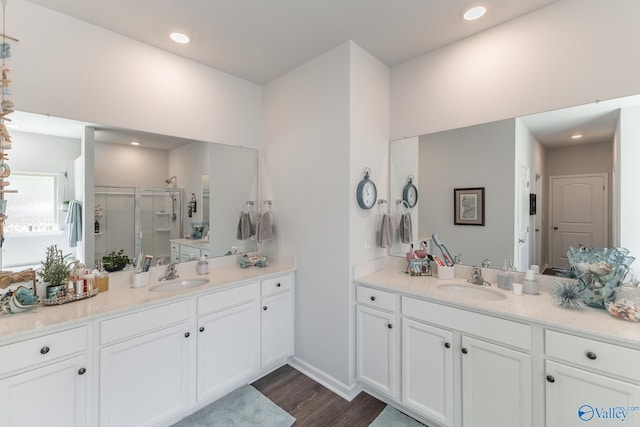 full bath featuring a shower stall, two vanities, wood finished floors, and a sink