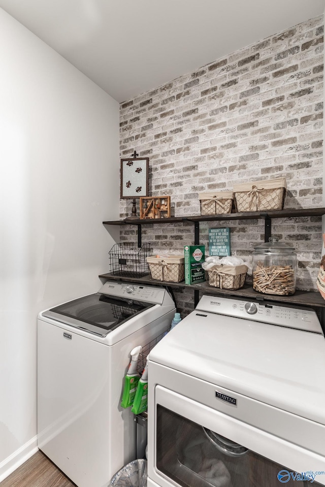 laundry room with brick wall, wood finished floors, washer and dryer, and laundry area