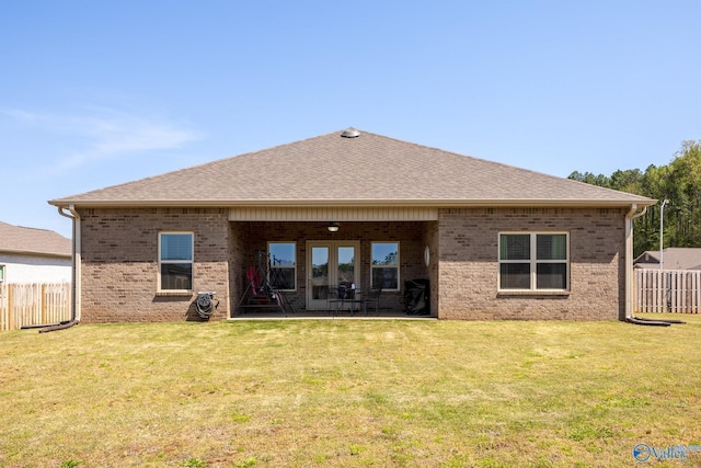 rear view of house with roof with shingles, fence, brick siding, a lawn, and a patio