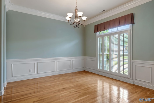 empty room with a notable chandelier, visible vents, light wood-style floors, ornamental molding, and wainscoting