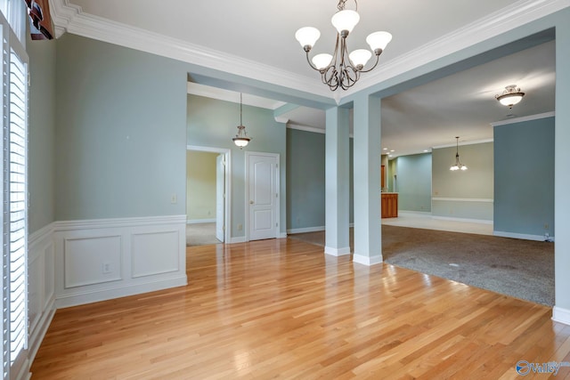 empty room with a chandelier, a wainscoted wall, ornamental molding, and light wood finished floors