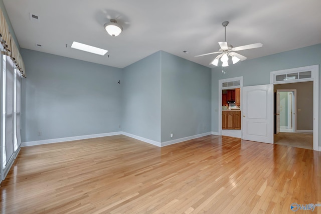 unfurnished room featuring ceiling fan, light wood-type flooring, a skylight, and baseboards