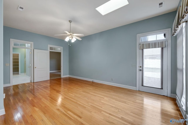 empty room featuring a skylight, baseboards, visible vents, and light wood finished floors