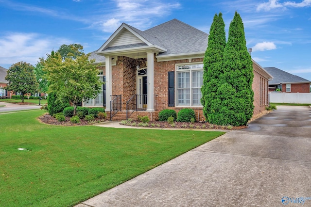 view of front of house featuring roof with shingles, a front yard, and brick siding