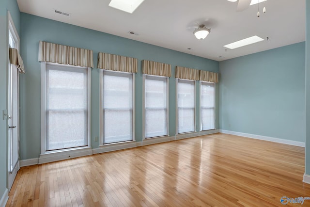 empty room with light wood-type flooring, a skylight, baseboards, and visible vents