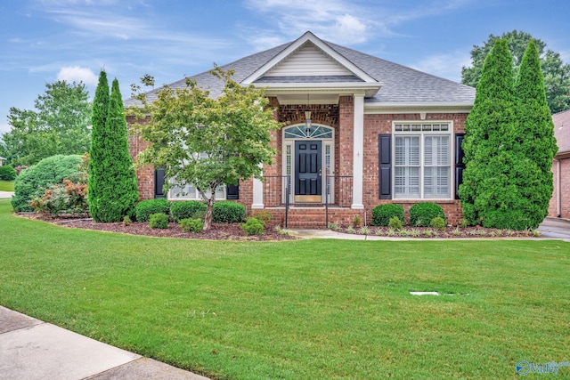 view of front of property featuring a shingled roof, a front yard, and brick siding