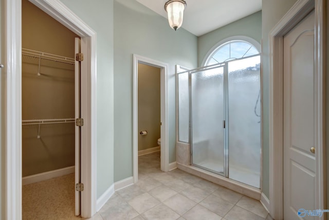 bathroom featuring a walk in closet, toilet, a shower stall, and baseboards