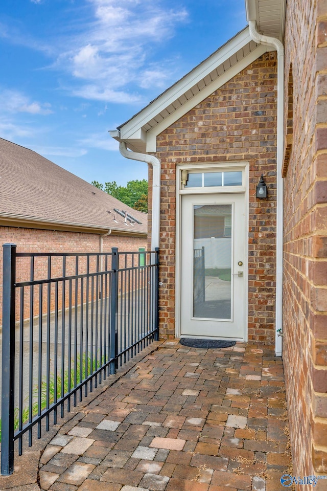 view of exterior entry featuring fence and brick siding