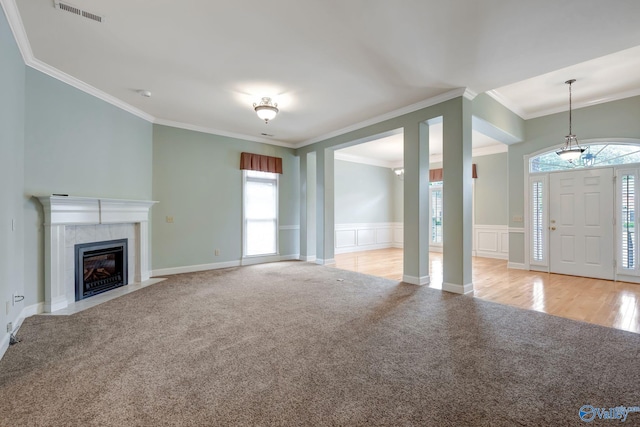 unfurnished living room with light carpet, visible vents, a tile fireplace, a wainscoted wall, and crown molding