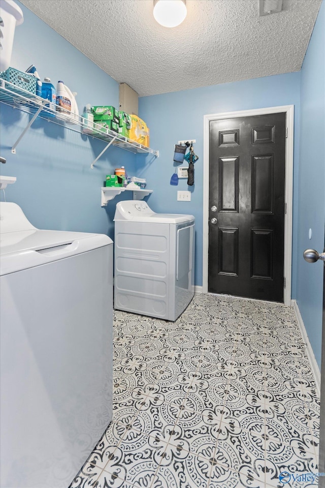 clothes washing area with washer and dryer, light tile patterned floors, and a textured ceiling