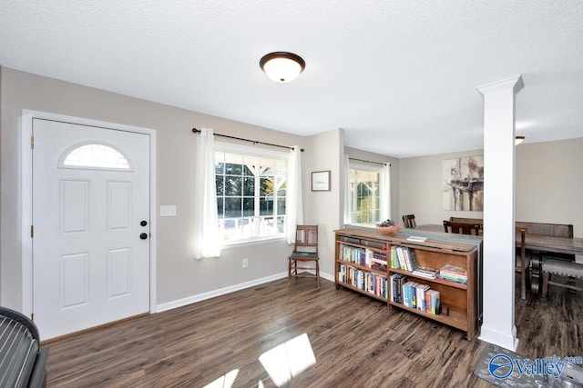 foyer entrance with dark hardwood / wood-style floors, a textured ceiling, and ornate columns