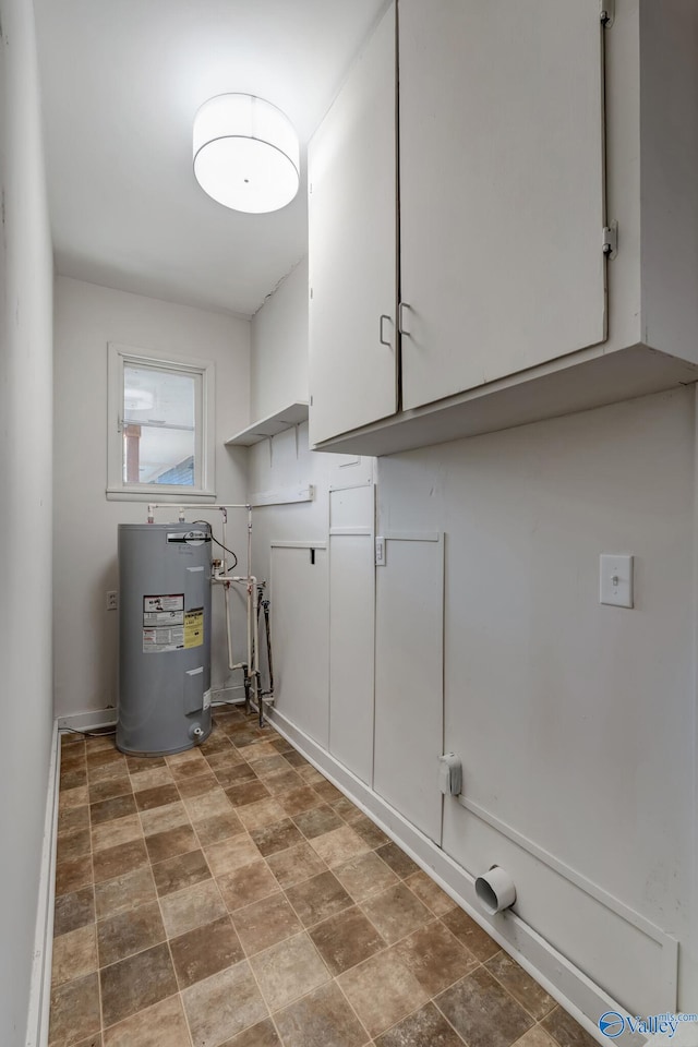 laundry area with stone finish floor, water heater, and cabinet space